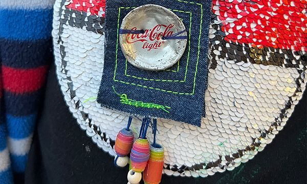 Nahaufnahme einer Paillettenhandtasche mit einem Coca-Cola-Flaschenverschluss, einem Jeansquadrat und Perlenquasten.