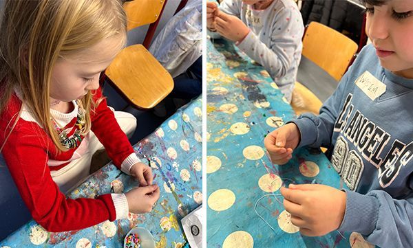 Zwei Kinder an einem Basteltisch, die Perlen auffädeln, konzentrierter Blick.