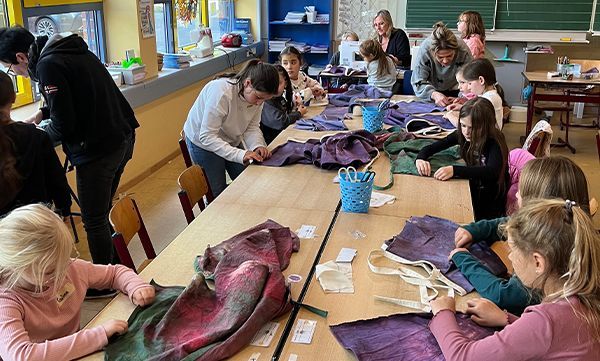 Schüler und Erwachsene nähen an einem langen Tisch in einem Klassenzimmer Stoff.