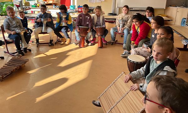 Kinder im Kreis spielen Perkussionsinstrumente: Xylophon, Trommeln. Helle Klassenzimmerumgebung.