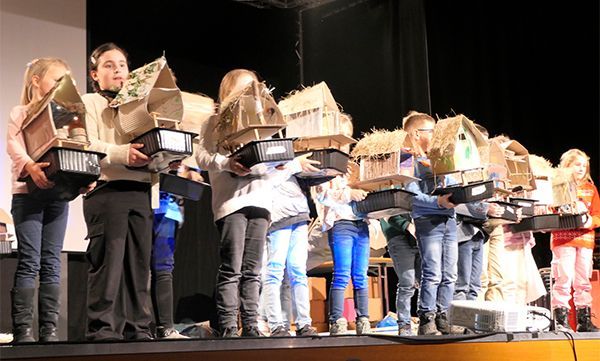 Kinder halten Vogelhäuser auf einer Bühne, möglicherweise eine Schulpräsentation.