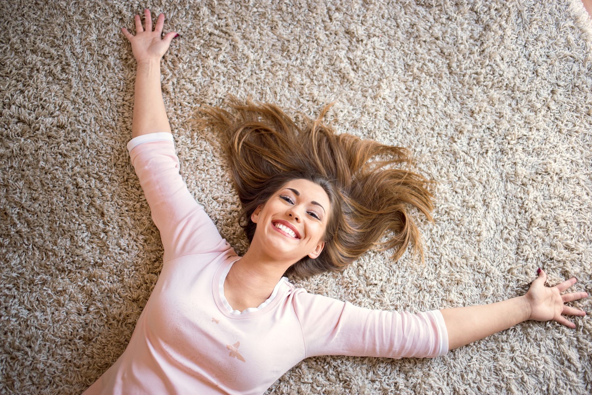 Woman lying on a carpet with arms outstretched, smiling and looking up.