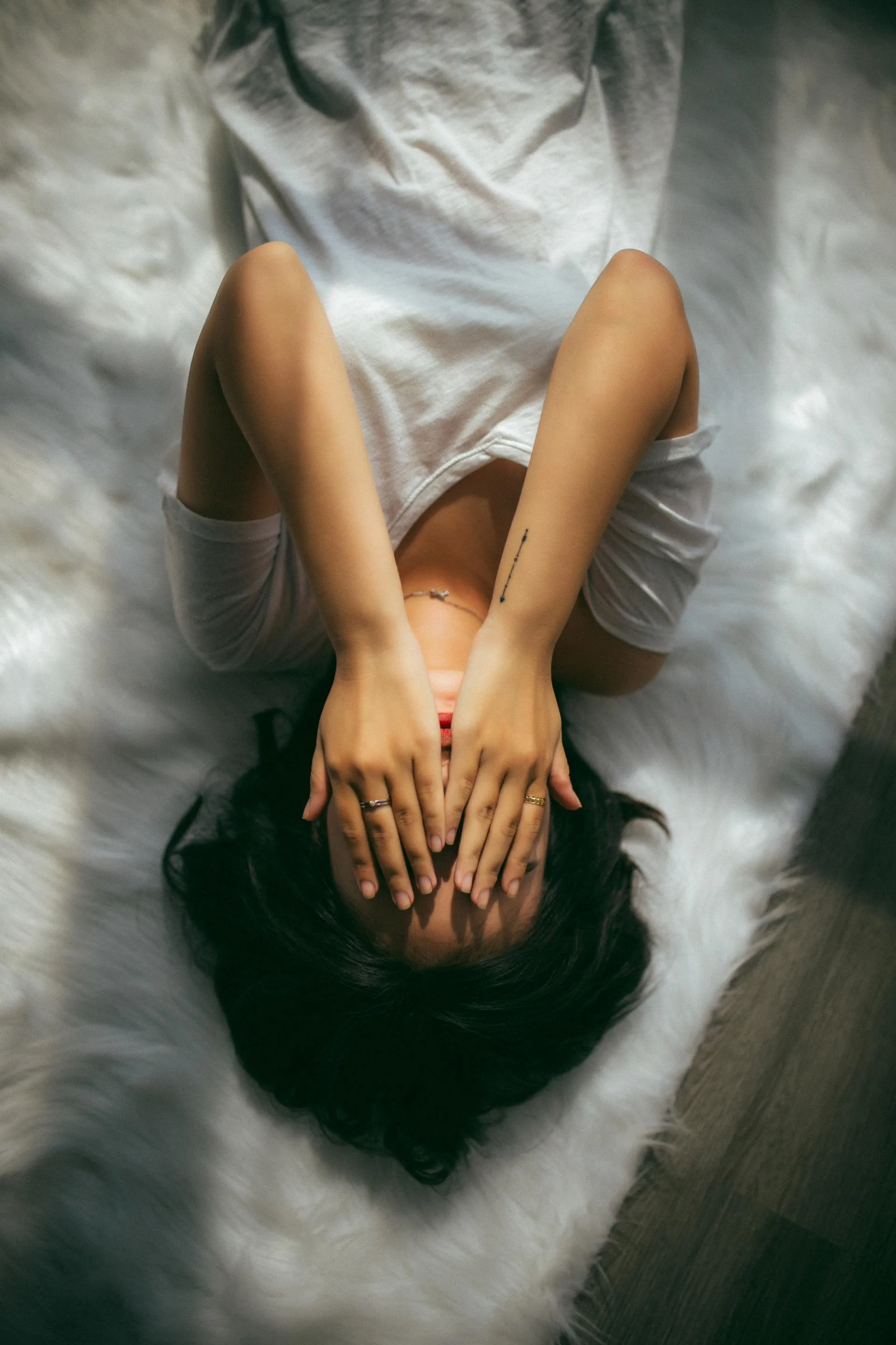 Vrouw ligt op een witte vacht, haar handen bedekken haar ogen