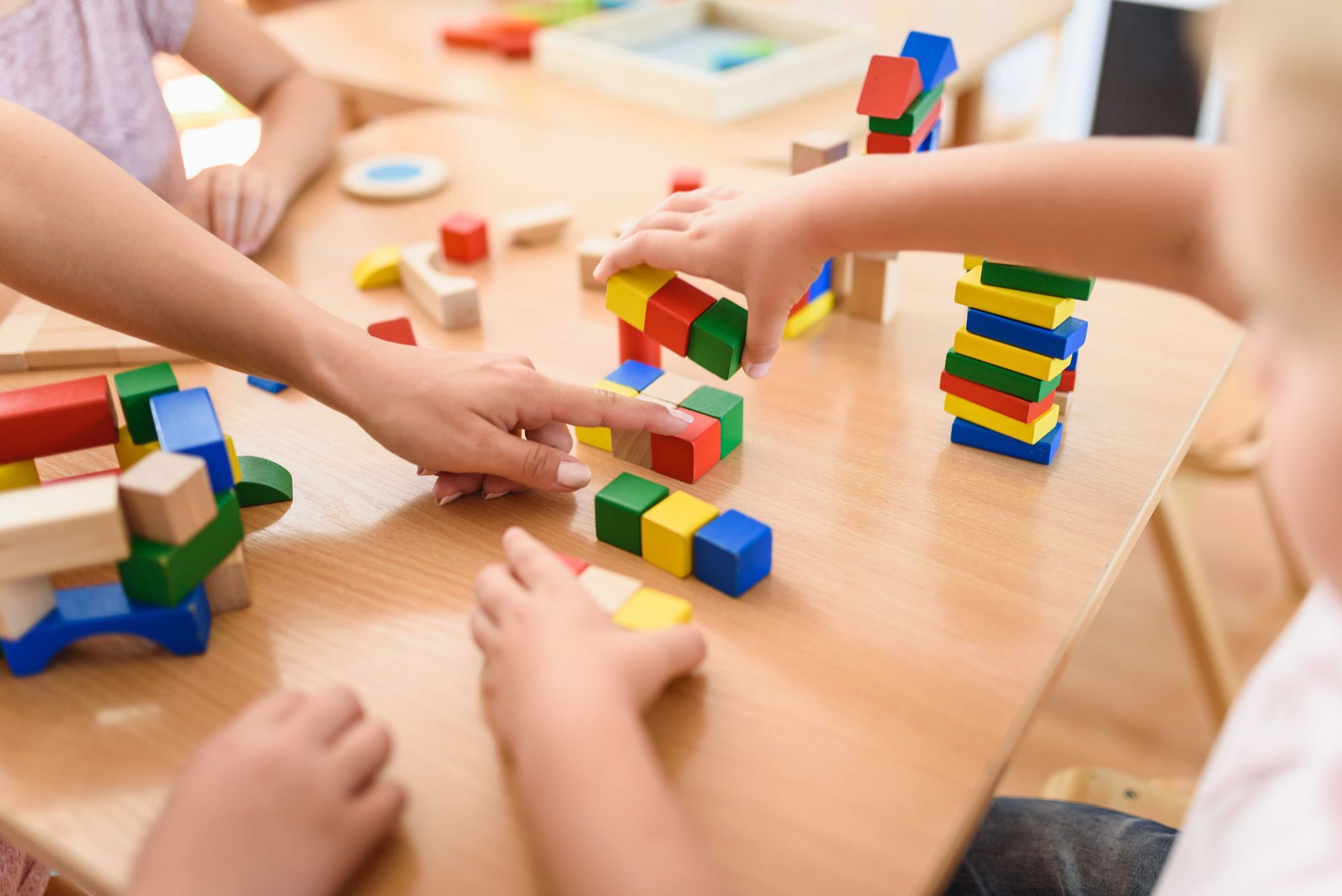 Des enfants construisent des tours et des structures colorées avec des blocs sur une table pendant la récréation.