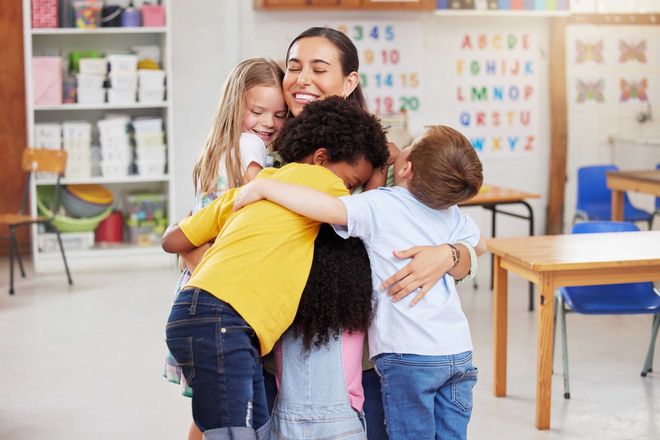 Une enseignante enlaçant trois enfants dans une salle de classe colorée
