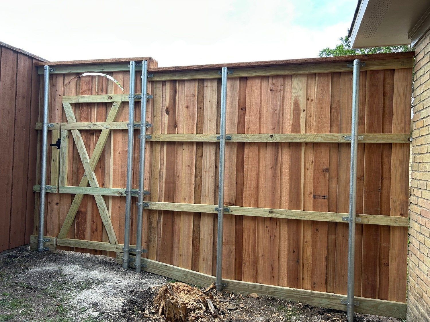 Wooden backyard fence with a gate and metal posts on a gravel area.