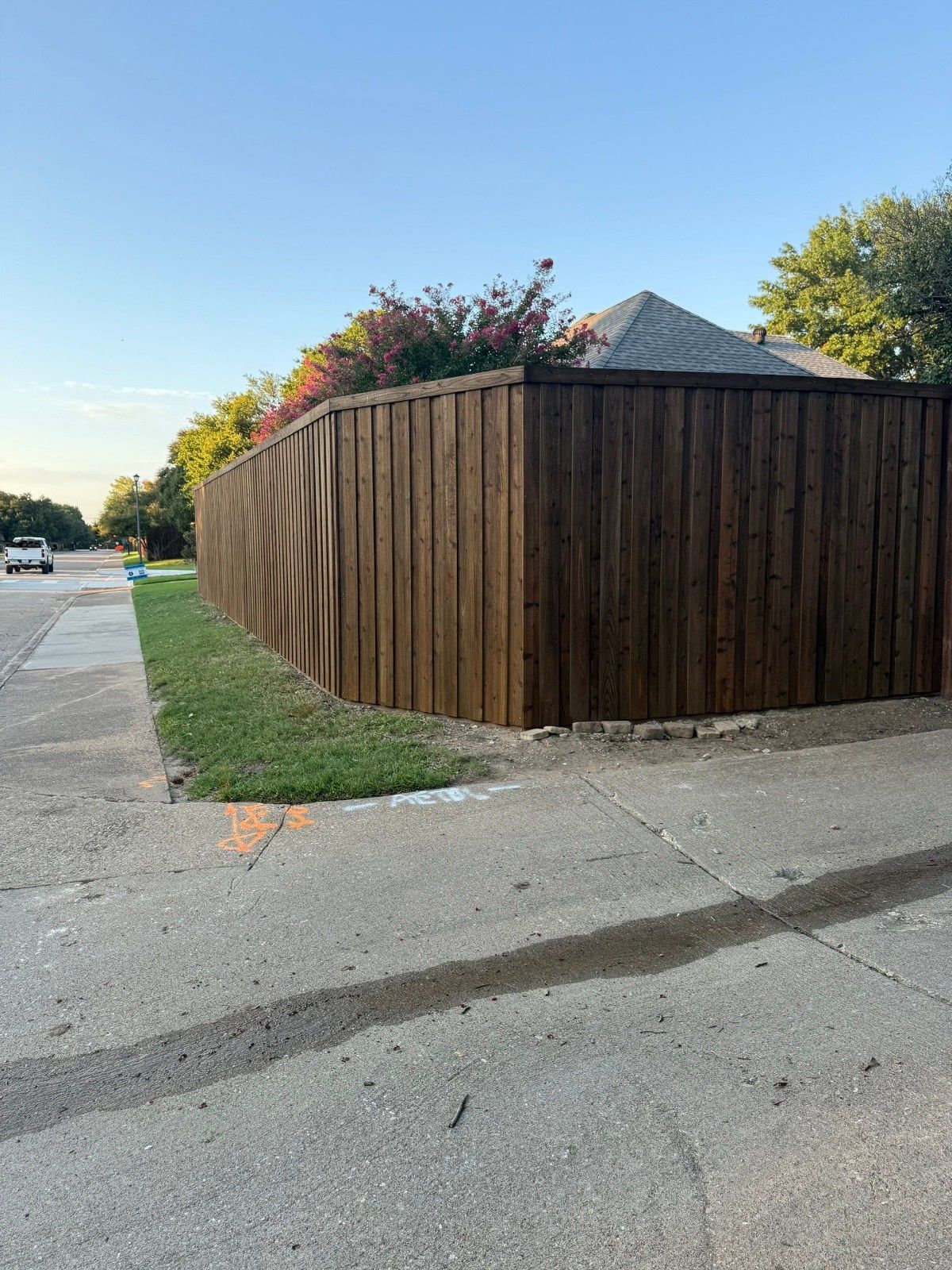 Wooden privacy fence curving around a corner lot beside a sidewalk and street at dusk.