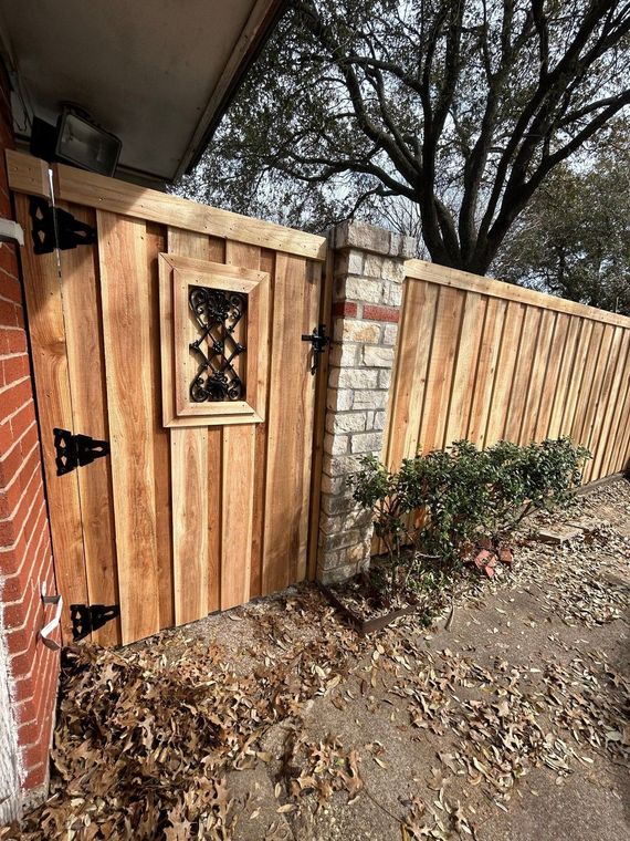 Wooden gate with decorative window beside a brick house and stone fence in a leaf-covered yard