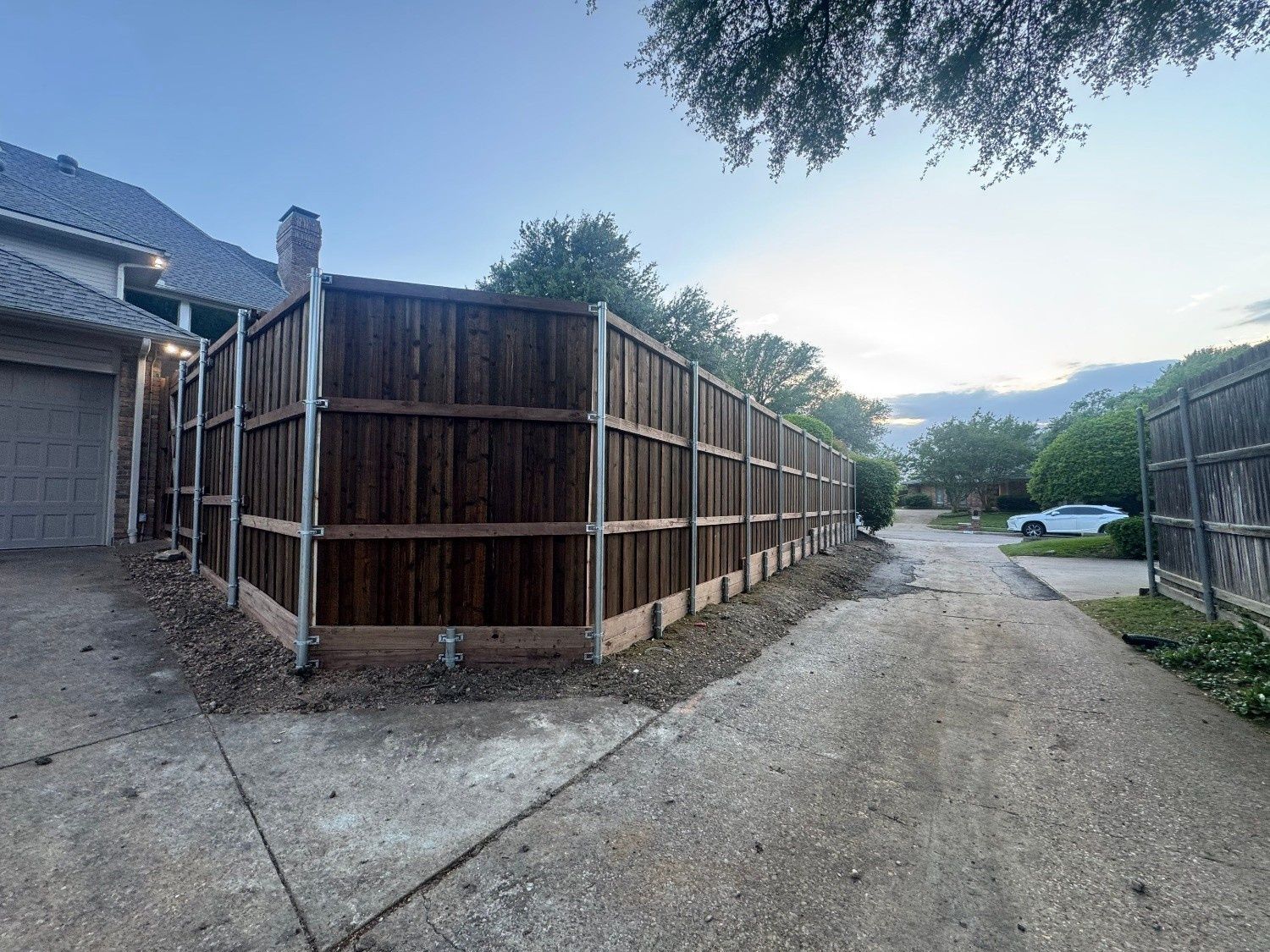 Wooden privacy fence beside a driveway in a suburban neighborhood at dusk