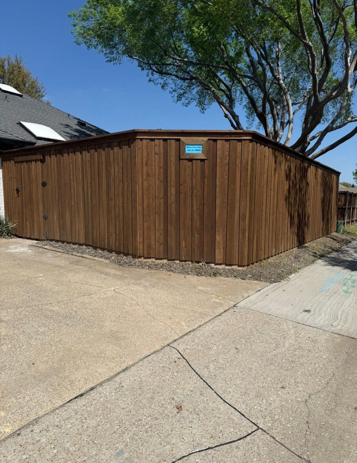 Wooden fence-lined side yard beside a sidewalk and driveway under a blue sky