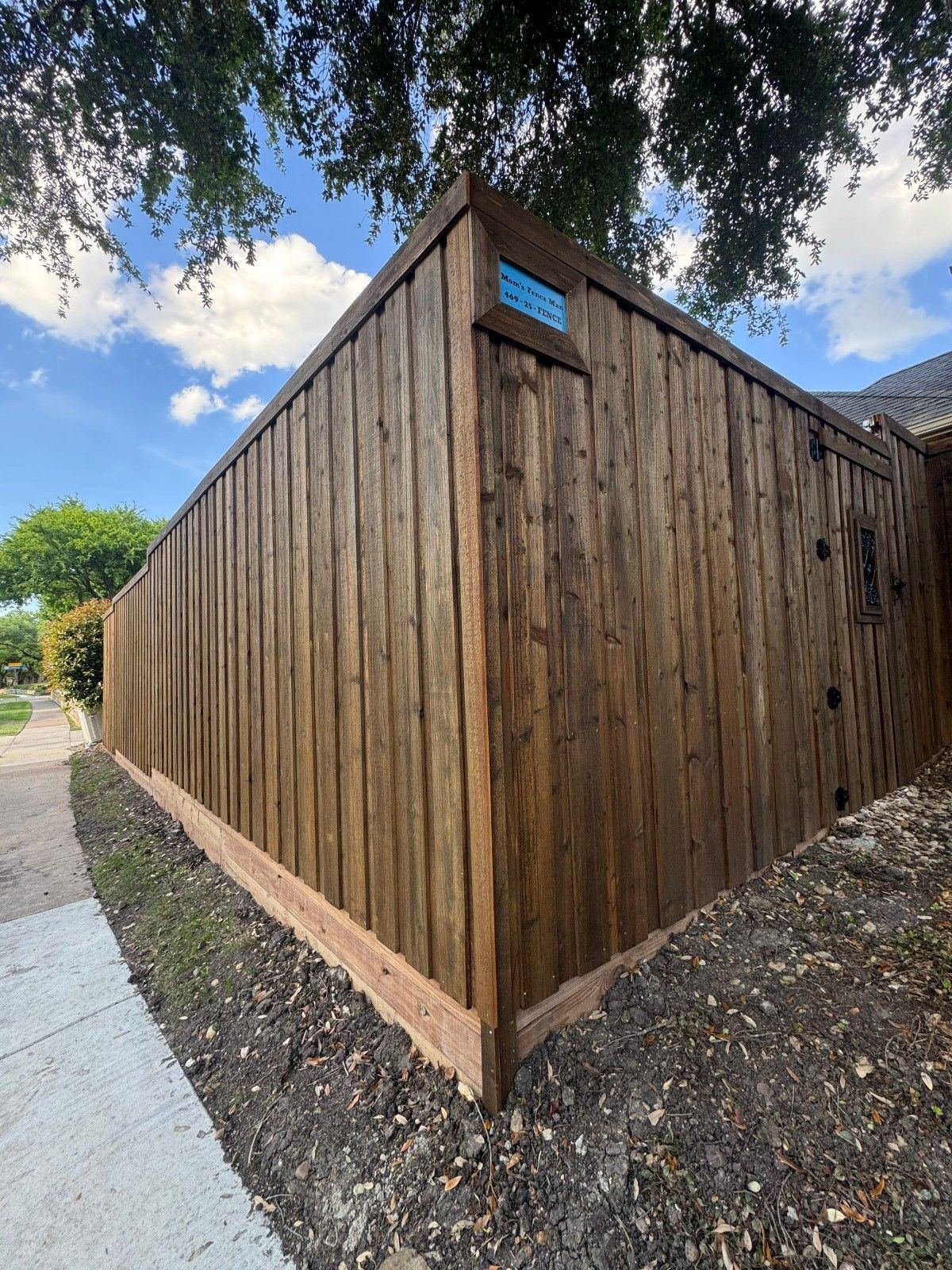 Wooden-sided building with a sloped roof beside a sidewalk and dirt path under a blue sky.
