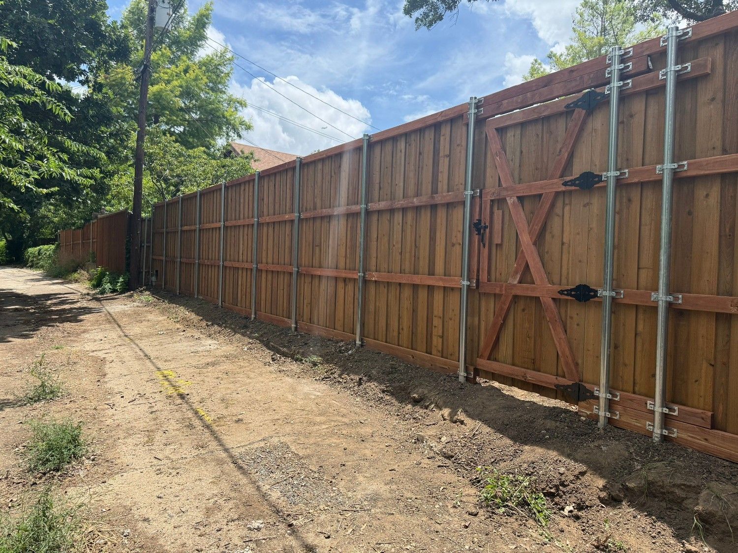 Long wooden fence lining a dirt path under a partly cloudy sky, with trees on the left.