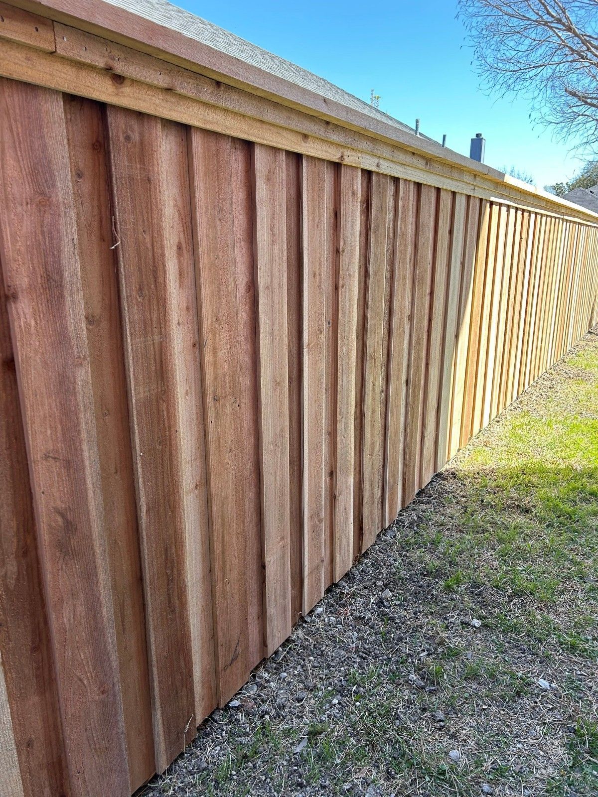 Long wooden fence beside a grassy yard under a clear blue sky