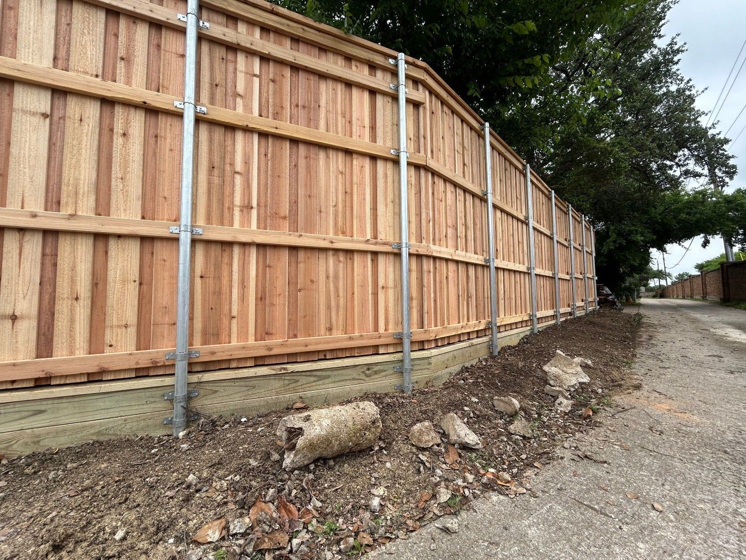Wooden privacy fence along a gravel road on a sloped dirt embankment