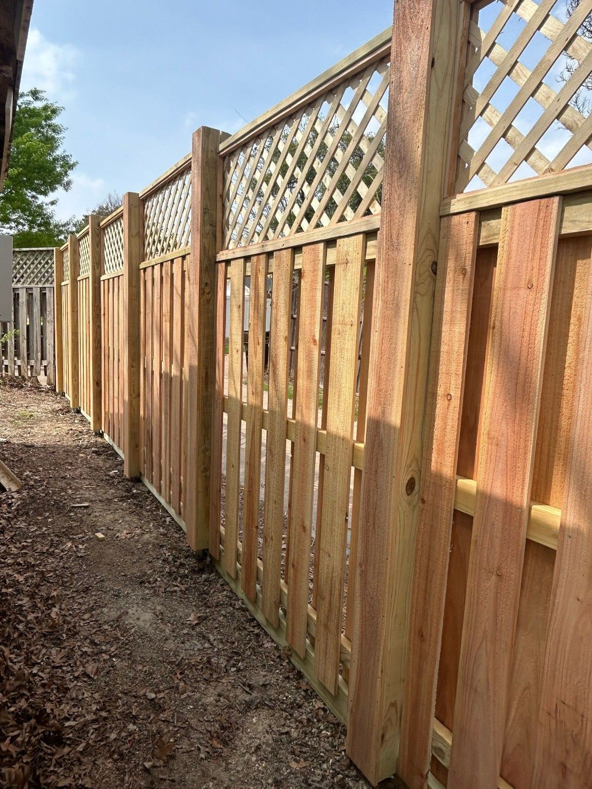Wooden privacy fence with lattice top along a dirt path beside a yard