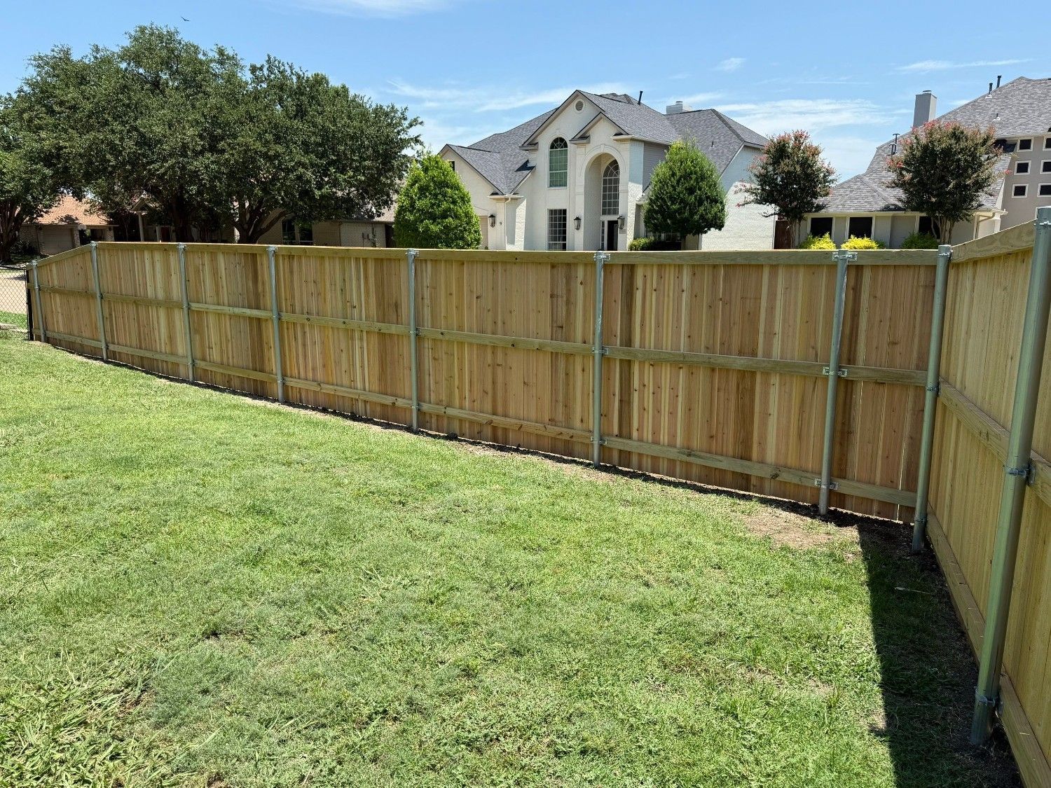 Backyard with green grass and a wooden privacy fence in front of suburban houses