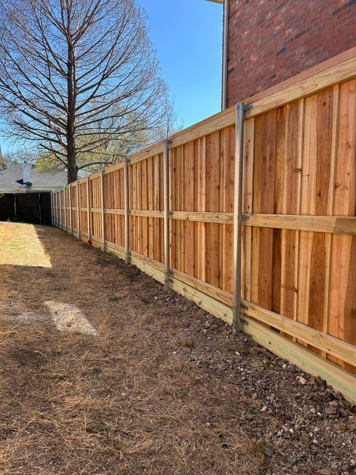 Wooden privacy fence beside a brick building along a grassy yard under a clear blue sky