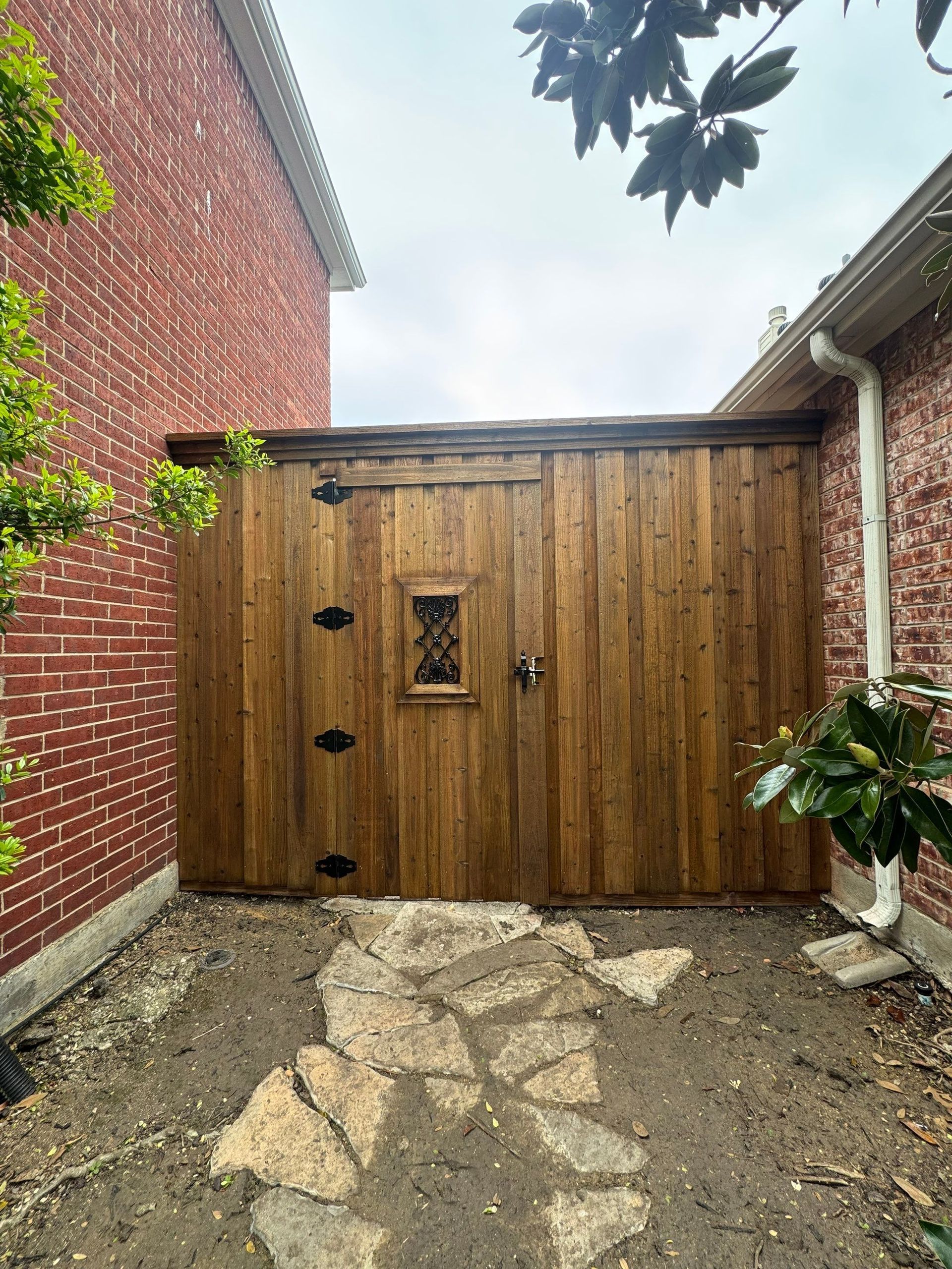 Wooden gate between brick walls with stone path and leafy branches overhead