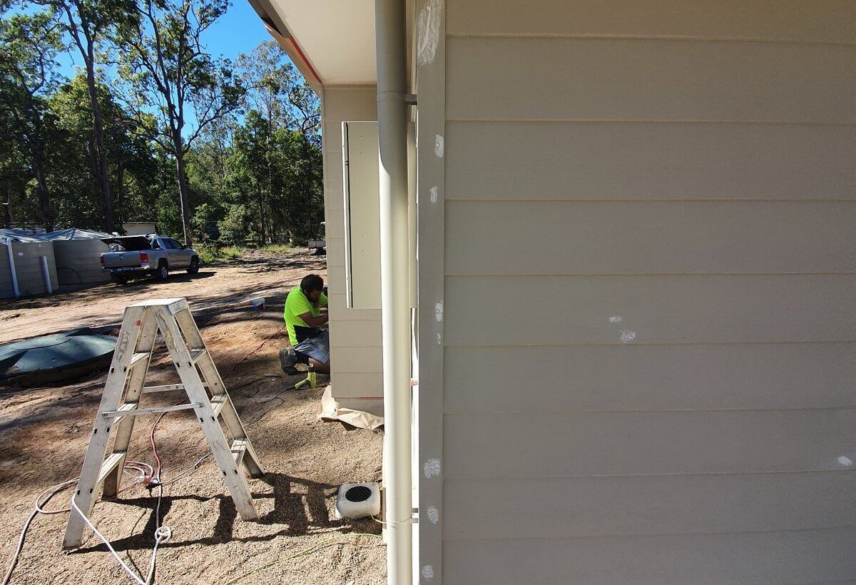 A Man Is Painting a Wall with A Paint Roller — A Brush With Colour in Urraween, QLD