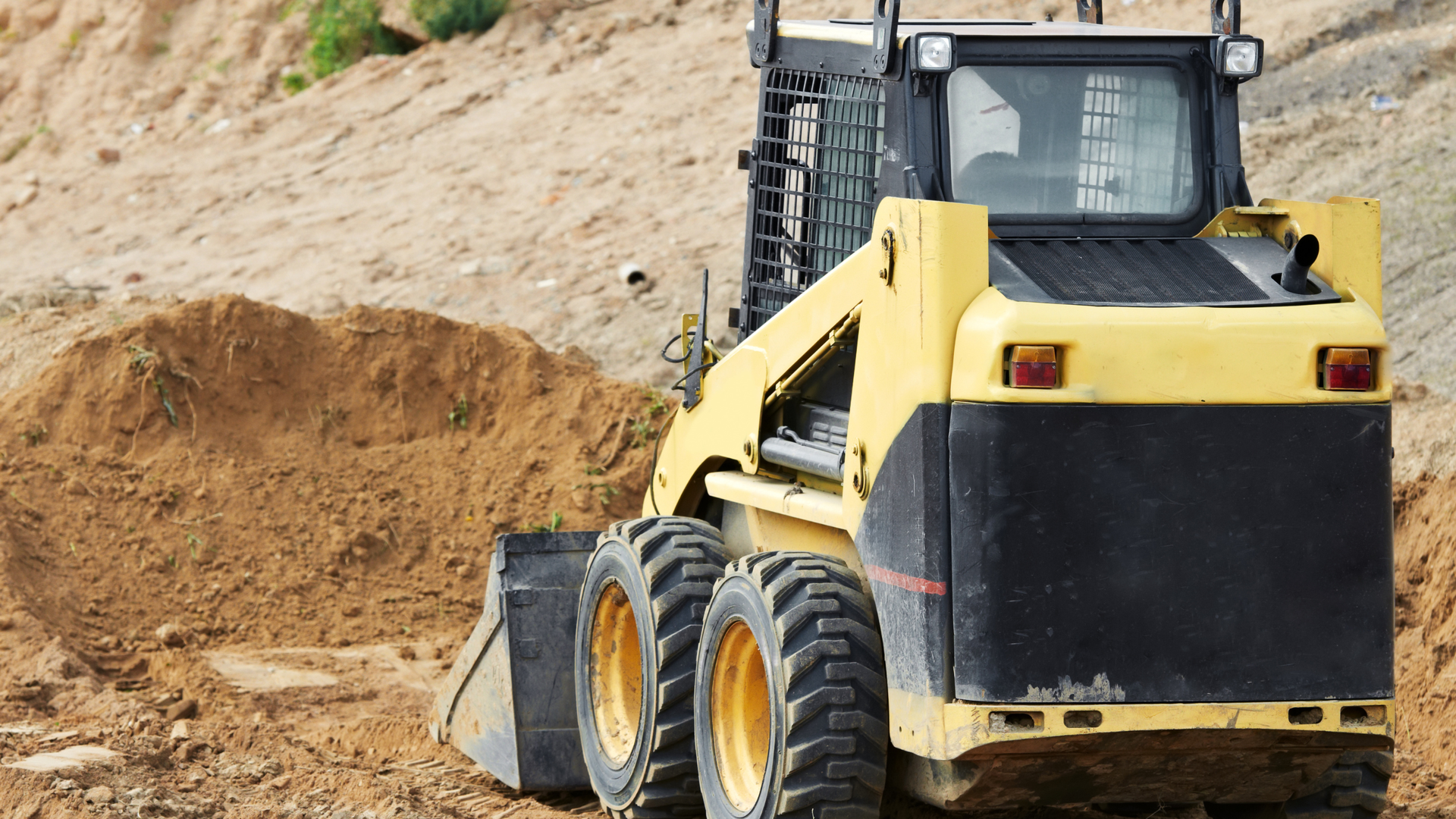 Yellow skid steer loader moving dirt at a construction site
