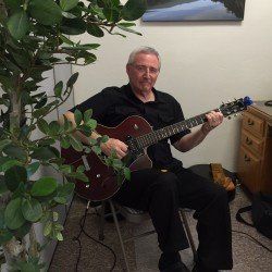 A man is sitting in a chair playing an electric guitar.