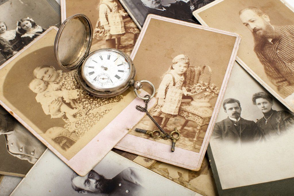 A pocket watch is sitting on top of a pile of old photographs