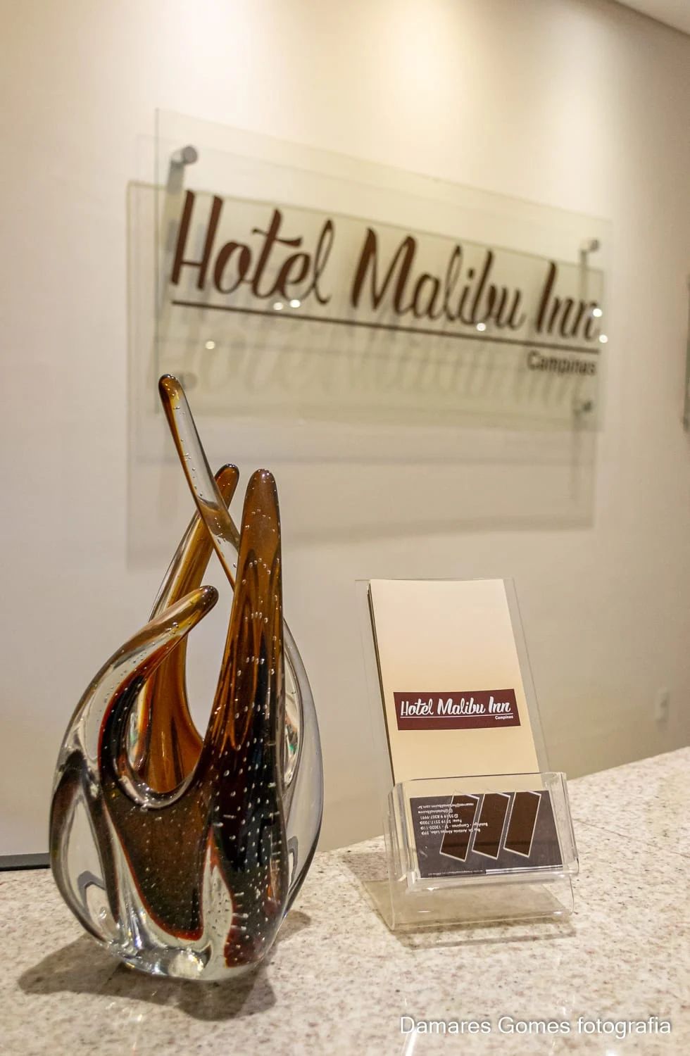 Um vaso de vidro está sobre um balcão em frente a uma placa que diz hotel malibu inn.-hotel-malibu-inn