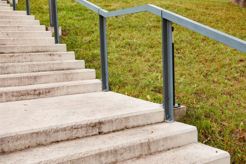 Concrete outdoor stairs with blue metal railings beside a grassy slope