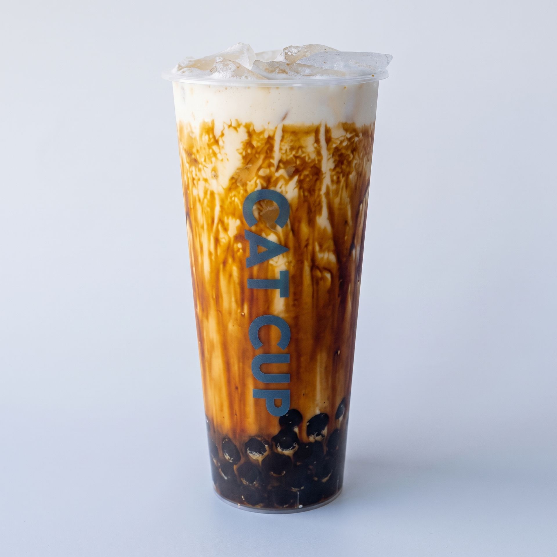 Tall iced bubble tea in a clear cup with blue CAT CUP text and dark tapioca pearls at the bottom