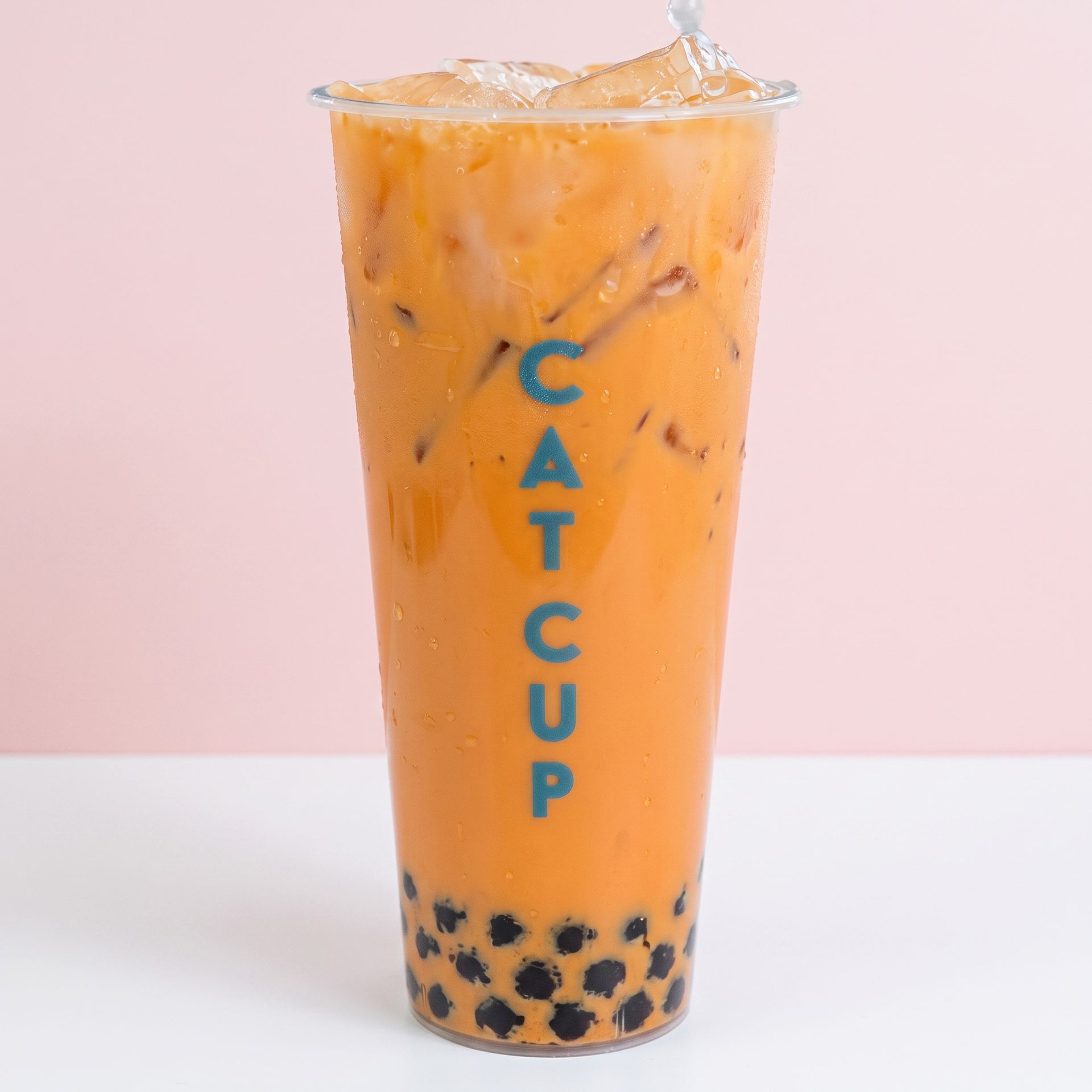 Tall orange bubble tea in a clear cup with black tapioca pearls and “CAT CUP” text