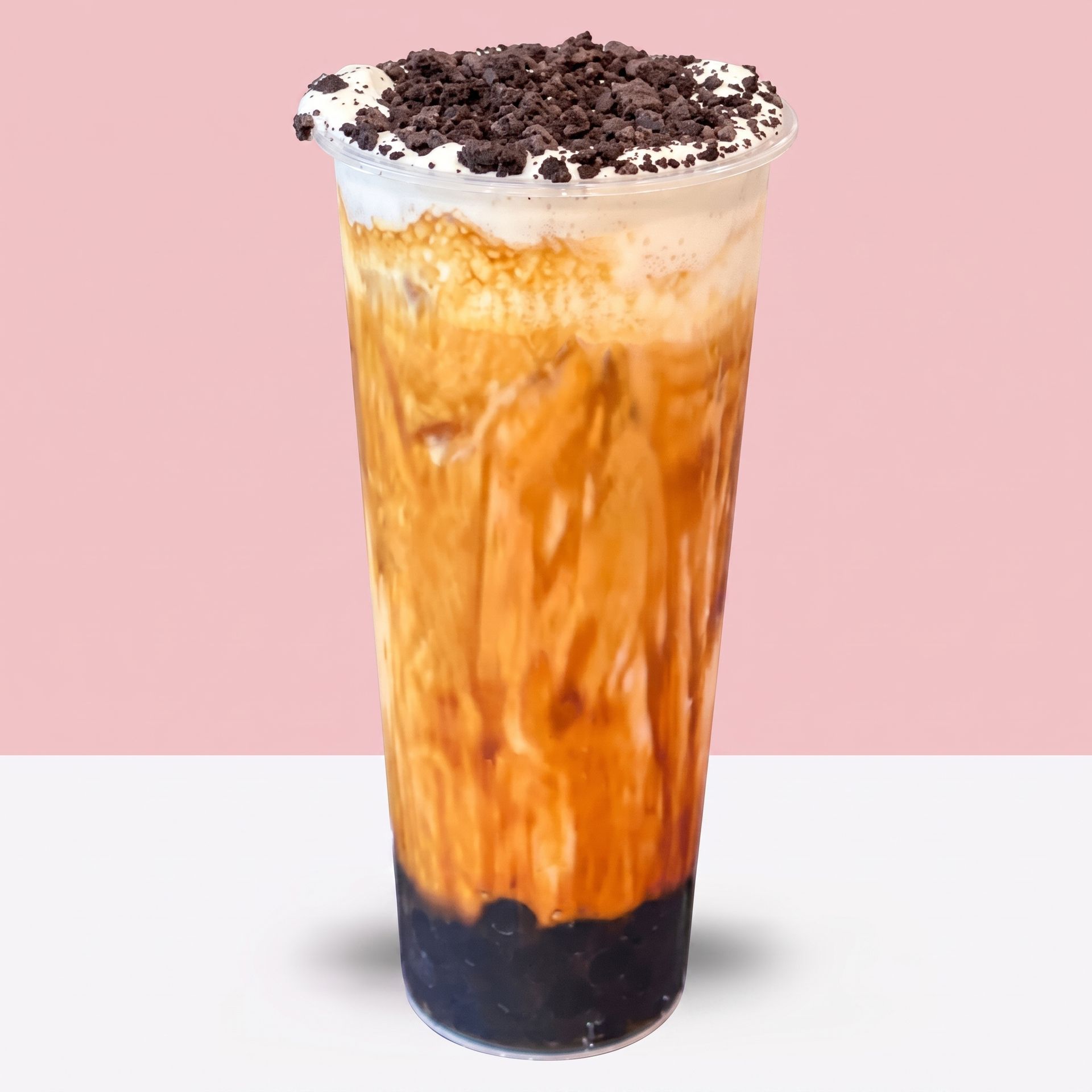 Tall iced coffee with orange swirls, whipped cream, and chocolate crumbs on top against a pink background