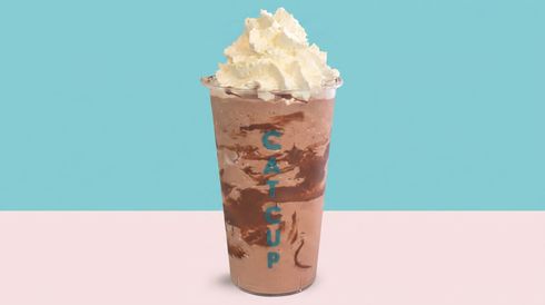 Tall iced drink in a brown cup topped with whipped cream against a blue and pink background