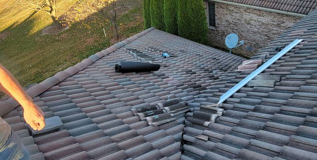Person on a tiled roof near chimney and antenna; daytime.