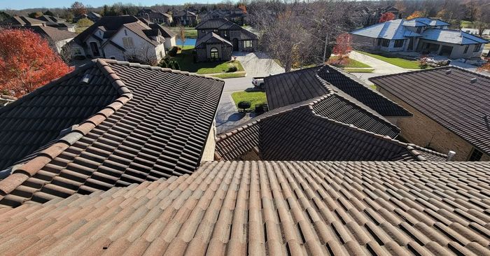 View from a tile roof overlooking a neighborhood with similar roofs, green lawns, and trees.