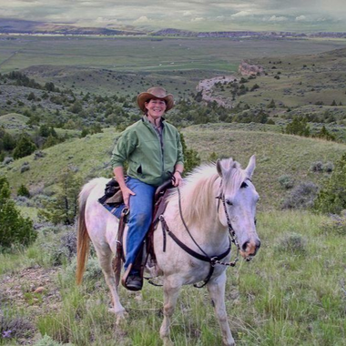 Person in a green shirt and cowboy hat riding a white horse on a grassy hillside.