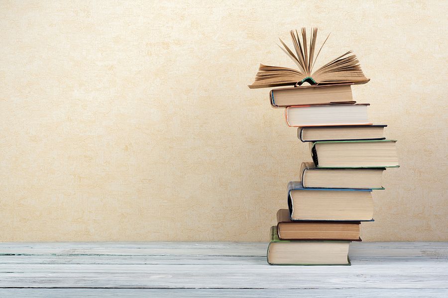 Stack of books with the top book open on a table.