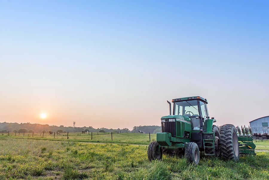 Agricultural landscape of a tractor in a field on a farm with the sun setting.