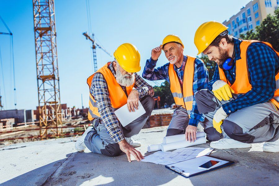 Construction work site with three workers with hard hats kneeling down reviewing site plans.