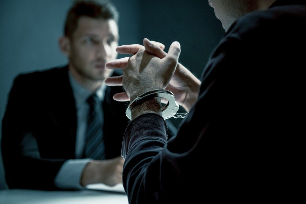 Man in Handcuffs at a Table, Facing Another Man in a Suit — Hannaway Lawyers in Port Macquarie, NSW