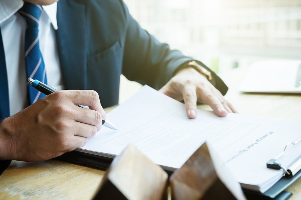 Man in Suit Signing Documents at a Wooden Table — Hannaway Lawyers in Port Macquarie, NSW