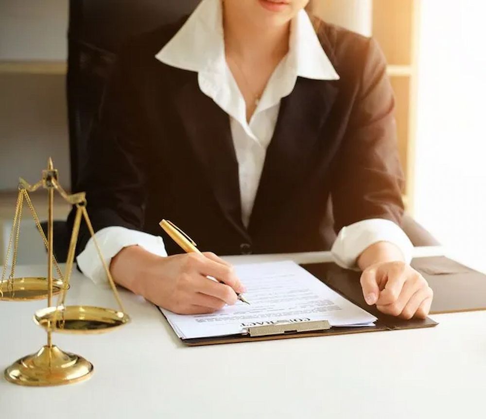 Woman in Black Suit Writing on a Document at a Desk, With Gavel and Scales — Hannaway Lawyers in Kempsey, NSW