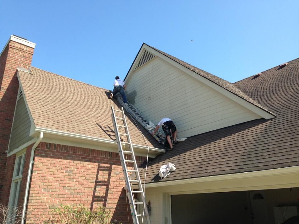 A man on a ladder is working on the roof of a house