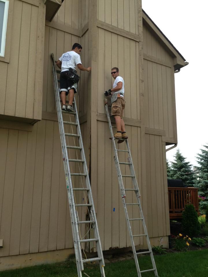 Two men are painting the side of a house with ladders