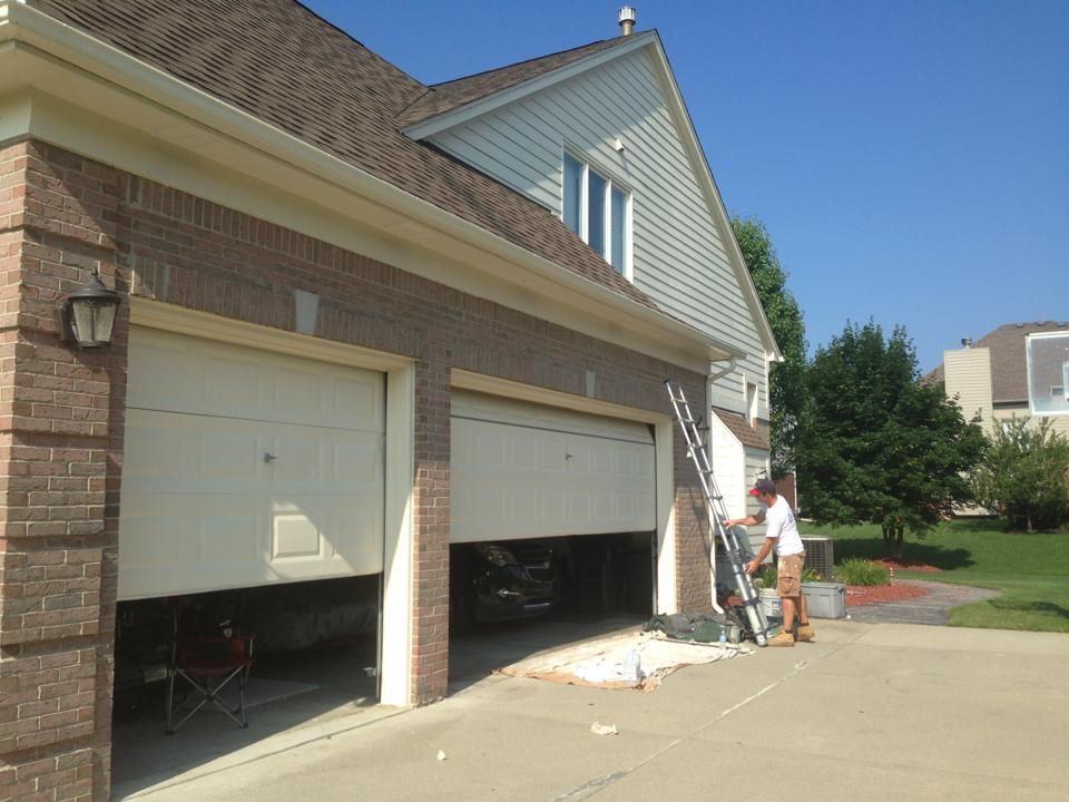 Two men are painting the side of a brick house