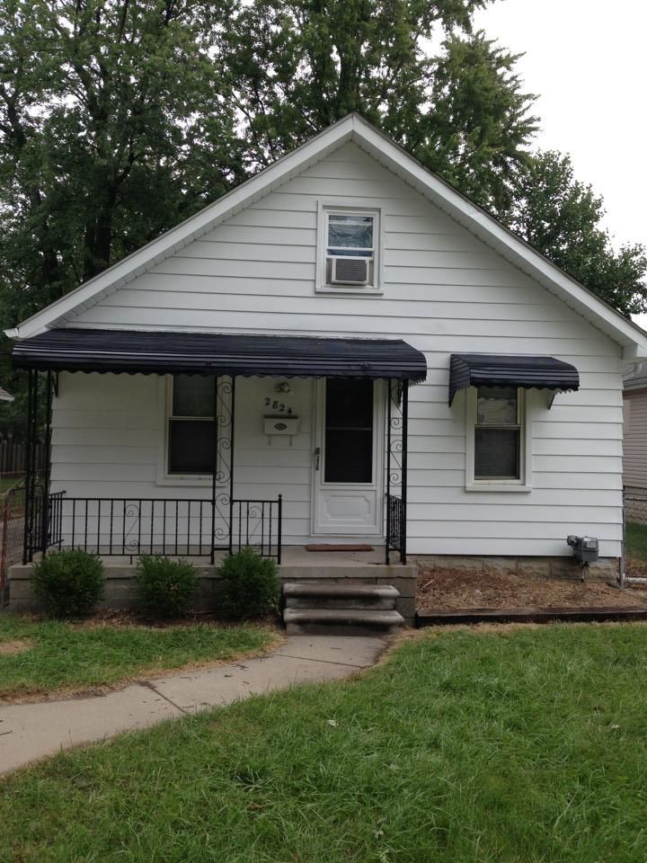 A small white house with a black awning on the porch.