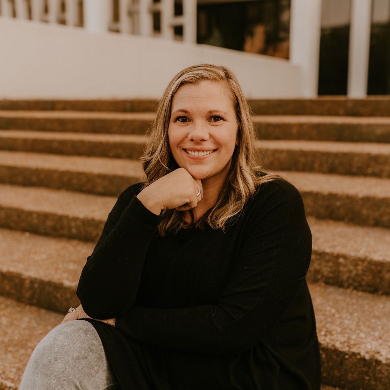 a woman in a black sweater is sitting on a set of stairs .