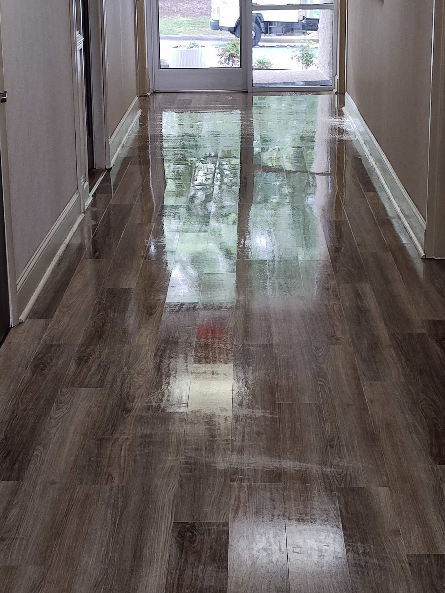 A long hallway with a shiny wooden floor and a door.