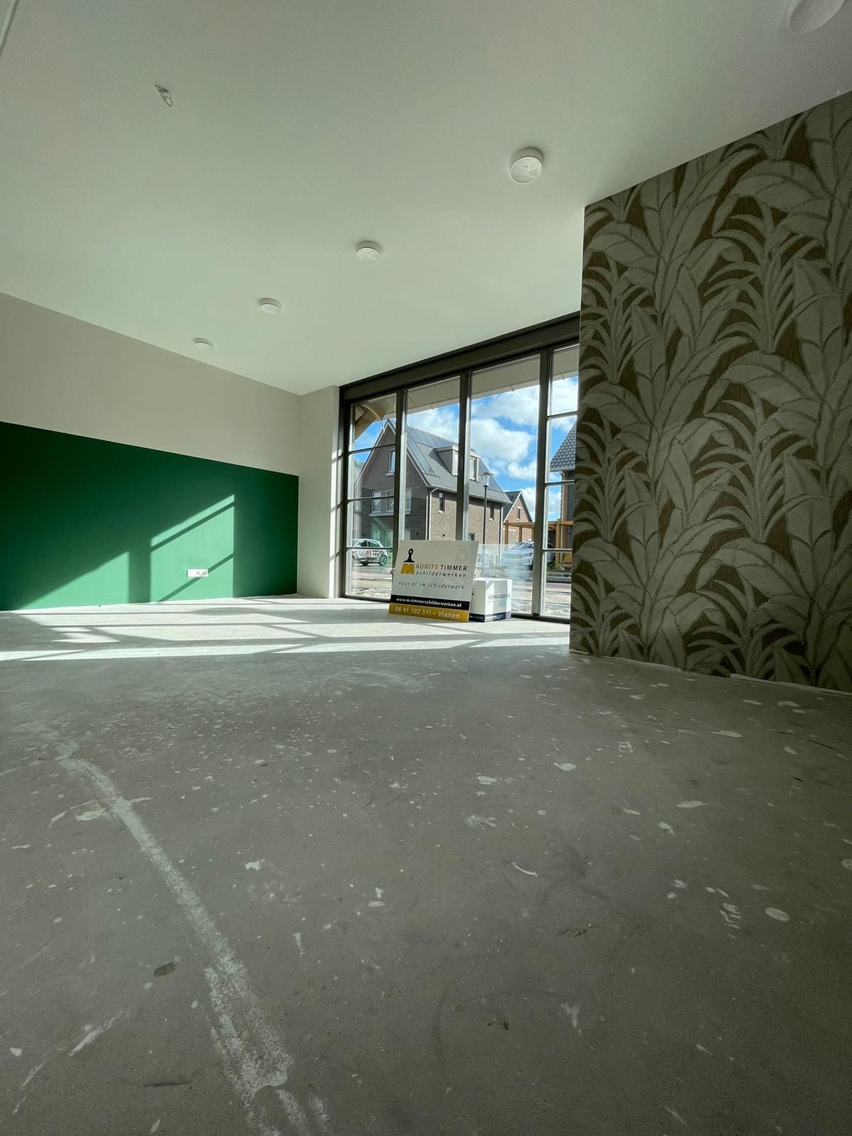 Lege kamer met een groene muur, behang met patroon en grote ramen die uitkijken op een gebouw.