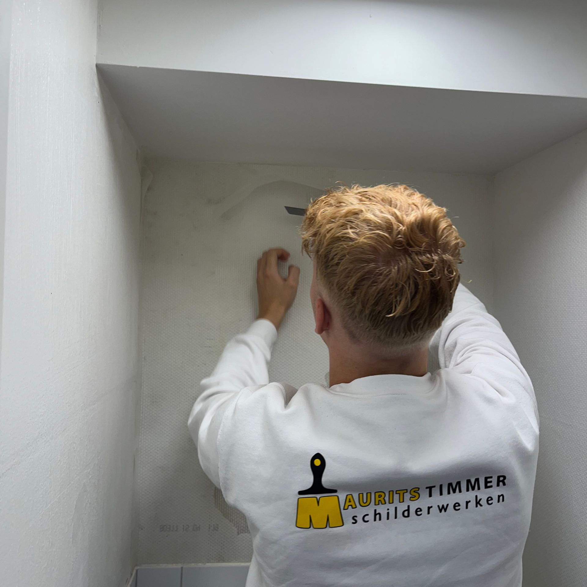 Man in wit overhemd brengt iets aan op een verdiepte muur; logo 