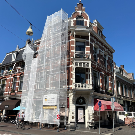 Hoekgebouw met steiger en bouwnet. Rode bakstenen gevel, straatbeeld.